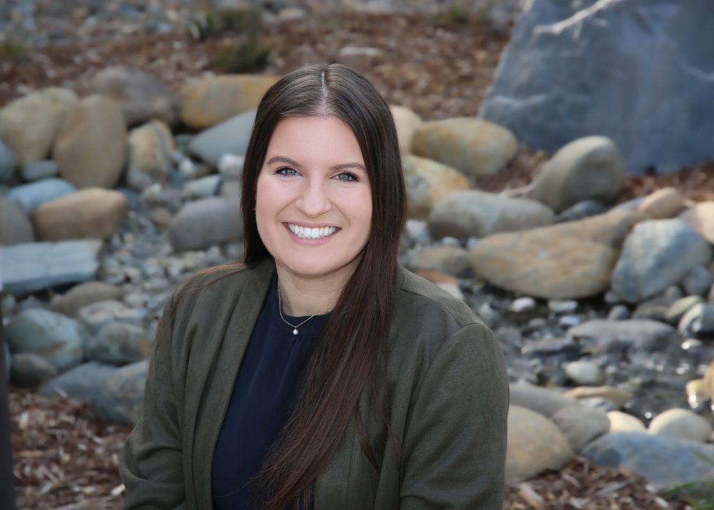 Portrait of a smiling woman with dark hair seated by a stream with rocks