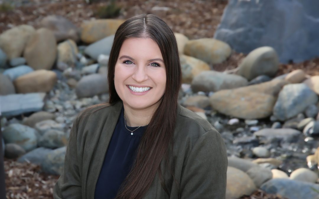 Portrait of a smiling woman with dark hair seated by a stream with rocks