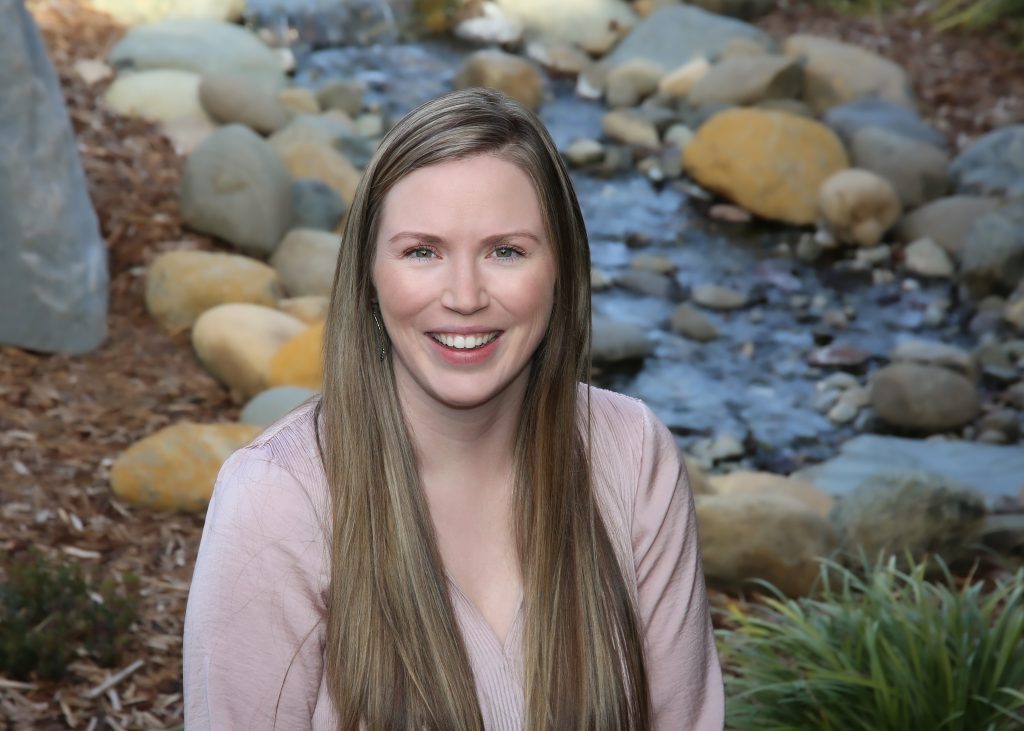 Portrait of a smiling woman with long hair seated by a stream with rocks