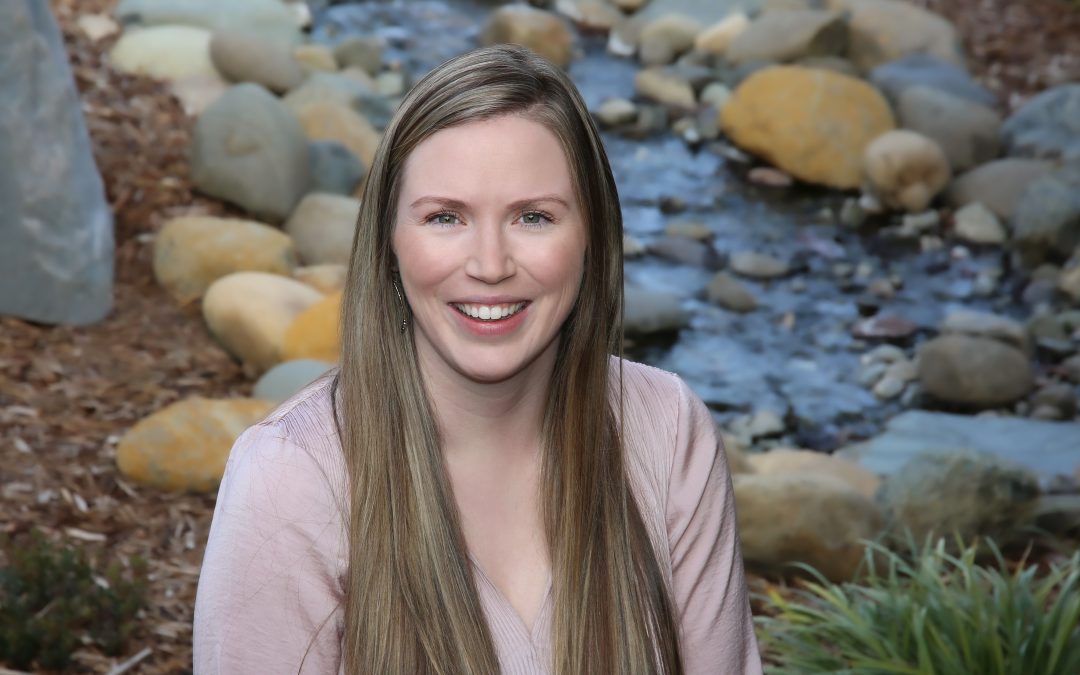 Portrait of a smiling woman with long hair seated by a stream with rocks