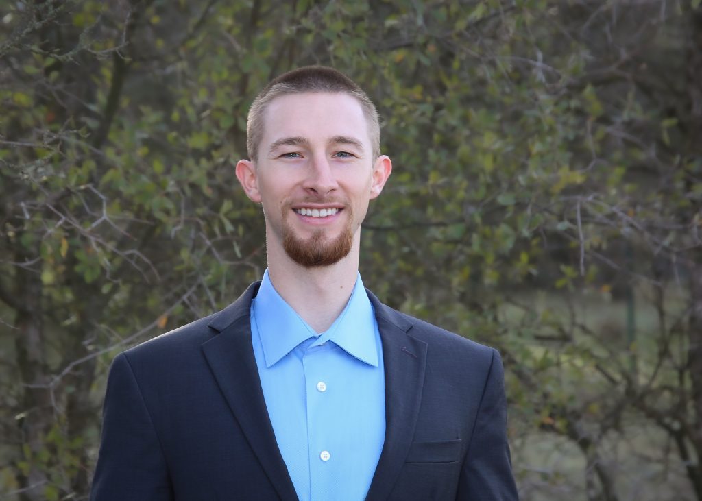 Young man in a suit smiling with trees in the background