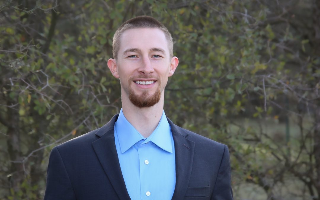 Young man in a suit smiling with trees in the background