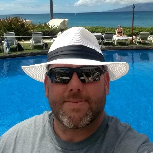 Man wearing a white hat and sunglasses by a pool with an ocean view