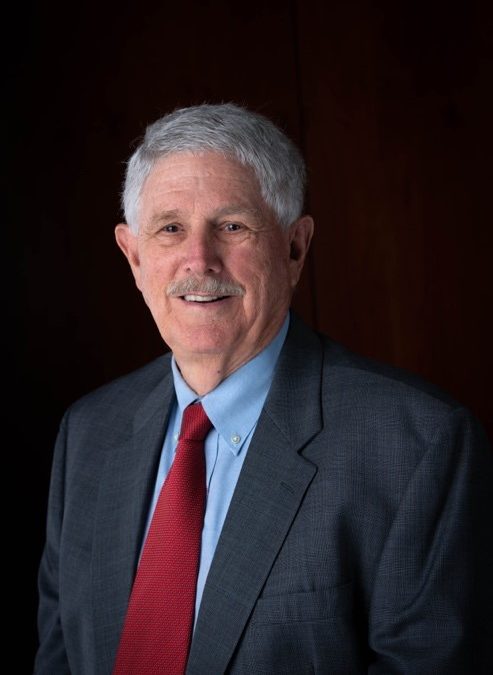 Professional headshot of a man in a gray suit with a red tie