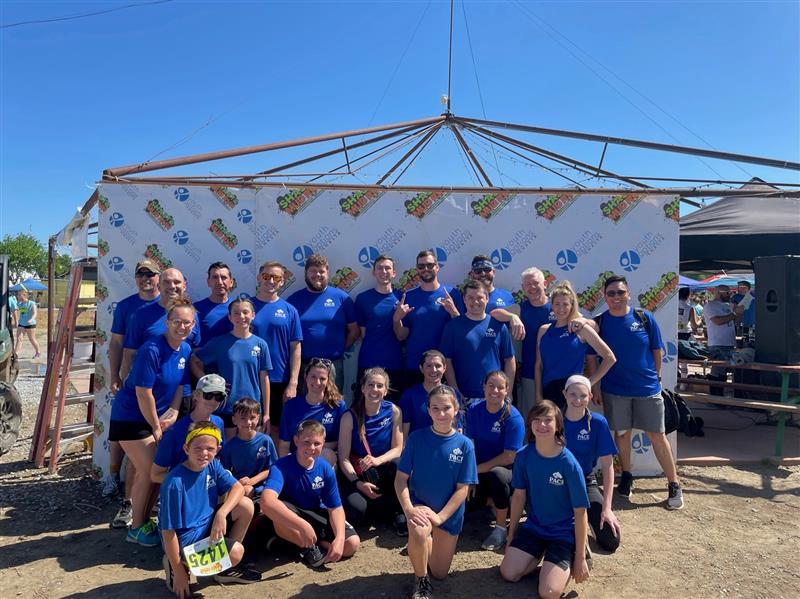 Team in blue shirts posing for a group photo in front of an event backdrop